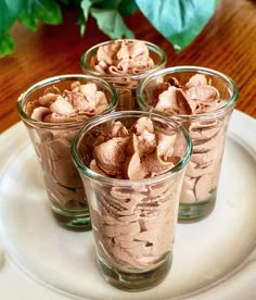 four glasses filled with dessert sitting on top of a white plate