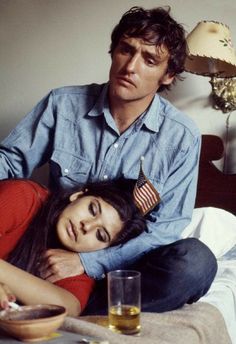 a man sitting next to a woman on top of a bed with an american flag