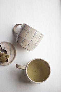 two coffee cups with spoons in them on a white table top next to each other