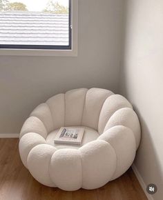 a white chair sitting in front of a window next to a book on top of a wooden floor