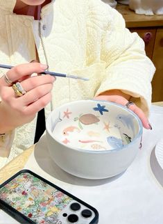 a woman sitting at a table with a bowl and spoon in front of her holding scissors