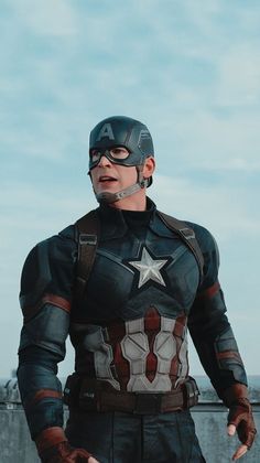 a man dressed as captain america standing in front of the ocean with his hands on his hips