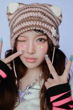 a girl with her fingers up to her face while wearing a hat and holding two fingers up in front of her face