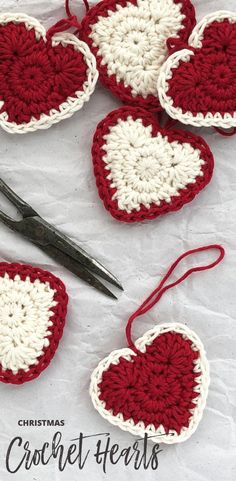 crocheted heart ornaments with scissors and thread on the table next to them are red and white