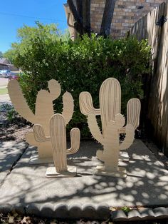 two wooden cactus sculptures sitting on top of a cement slab in front of a house