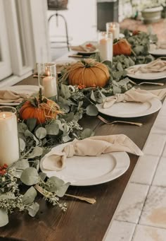 the table is set with pumpkins and greenery, candles and napkins on it