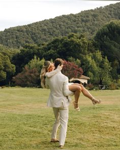 a man carrying a woman on his back in the middle of a field with trees behind him