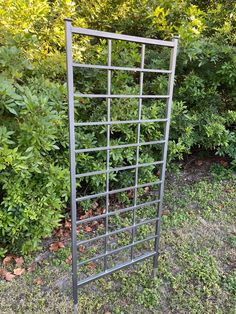 a metal trellis in the grass near bushes