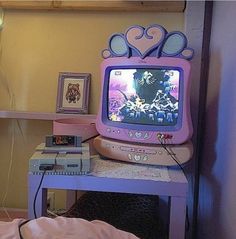 an old fashioned tv sitting on top of a purple table next to a pink bed