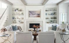 a living room filled with white furniture next to a fire place in a fireplace covered in bookshelves