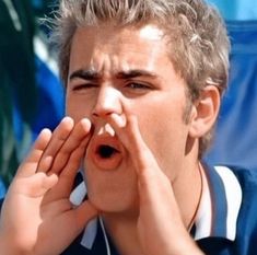 a young man holding his hands to his face while looking at something in front of him