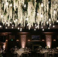 the ceiling is decorated with white flowers and hanging lights above it are round tables covered in tablecloths