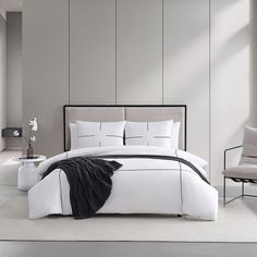 a bed with white sheets and black trims in a modern style bedroom, next to a chair