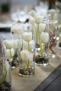 there are many vases with white flowers in them on the table cloth, along with rocks and pebbles