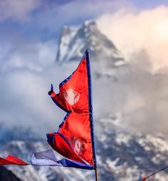 two red and blue flags flying in front of a snow covered mountainside with clouds