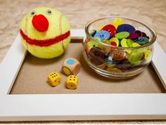 a glass bowl filled with lots of buttons next to a yellow ball and two wooden dices