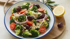 a salad with olives, broccoli and tomatoes in a bowl on a cutting board