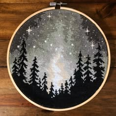 a cross stitch pattern with trees and stars in the night sky on a wooden surface