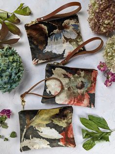 three small purses sitting on top of a table next to flowers and leaves,