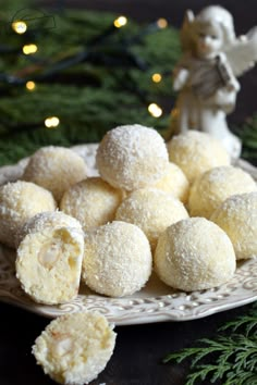 a white plate topped with snowball cookies next to a christmas tree and an angel figurine