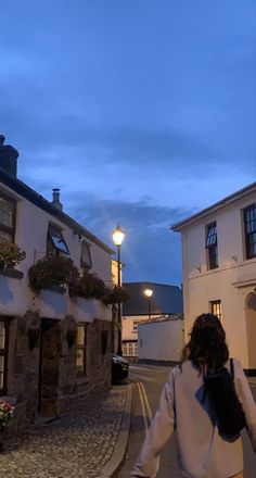 a woman is walking down the street in front of some buildings at dusk with her back to the camera