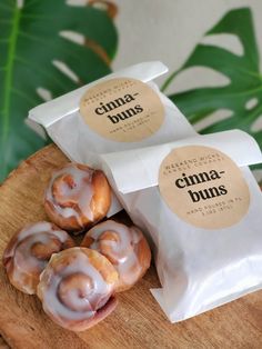 three cinnamon buns sitting on top of a wooden cutting board next to a bag