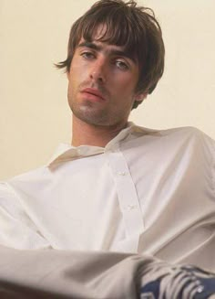 a man sitting on a bed with his feet propped up in the air and looking off to the side