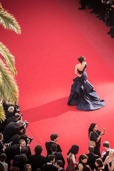 a woman in a blue dress standing on a red carpet next to people taking pictures