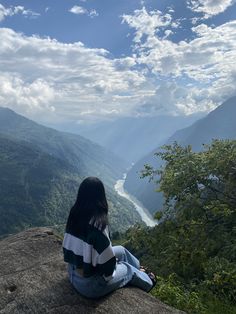 a woman sitting on top of a cliff overlooking a valley