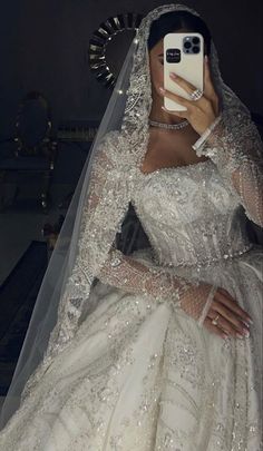 a woman in a wedding dress taking a selfie with her cell phone while wearing a veil