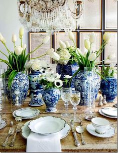 a dining room table set with blue and white dishes, silverware and flowers in vases