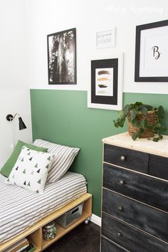 a small bedroom with green walls and black dressers in the foreground, white framed pictures on the wall