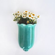 a blue vase with daisies in it hanging from the side on a white wall