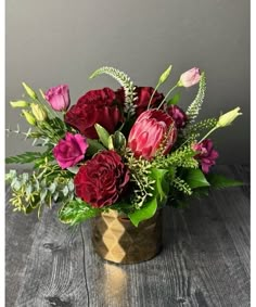 a vase filled with red and purple flowers on top of a wooden table next to a gray wall