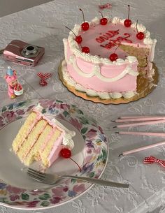 a pink and white cake sitting on top of a table next to a plate with a slice missing