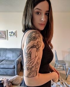 a woman with a tattoo on her arm standing in front of a couch and looking at the camera