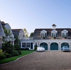 two classic cars parked in front of a large house with white trim and green shutters