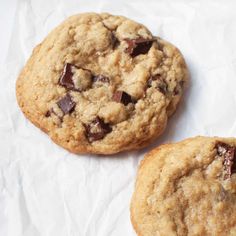 two chocolate chip cookies sitting on top of white paper