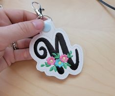 a hand holding a white and black keychain with flowers on it