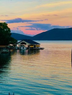 there is a boathouse on the water at sunset with mountains in the back ground