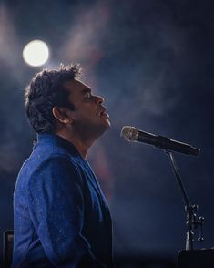 a man standing in front of a microphone on top of a stage with lights behind him