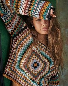 a woman with long hair wearing a multicolored crochet sweater and shorts