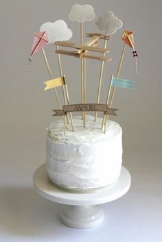 a white cake topped with lots of wooden sticks and flags in the shape of kites