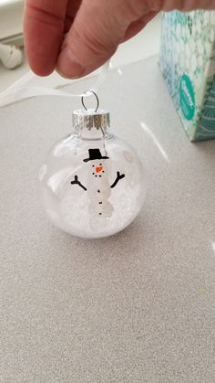 a hand holding a glass ornament with a snowman on it