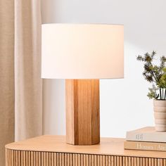 a table lamp sitting on top of a wooden dresser next to a book and potted plant