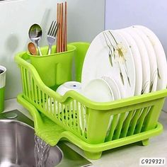 a green dish drainer filled with dishes and silverware next to a kitchen sink