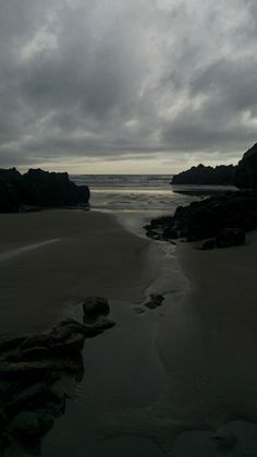 the beach is covered in sand and water under a cloudy sky, with rocks on either side