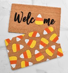 two door mats with candy corn on them and the words welcome written in black ink