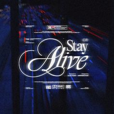 the words stay alive are in white and black letters on a dark background with blurry lights