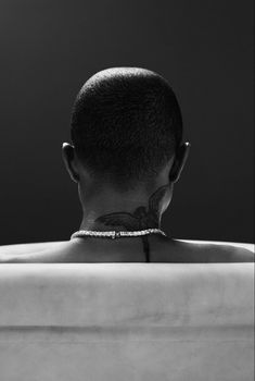 a man sitting in a bathtub with his back turned to the camera and wearing a necklace